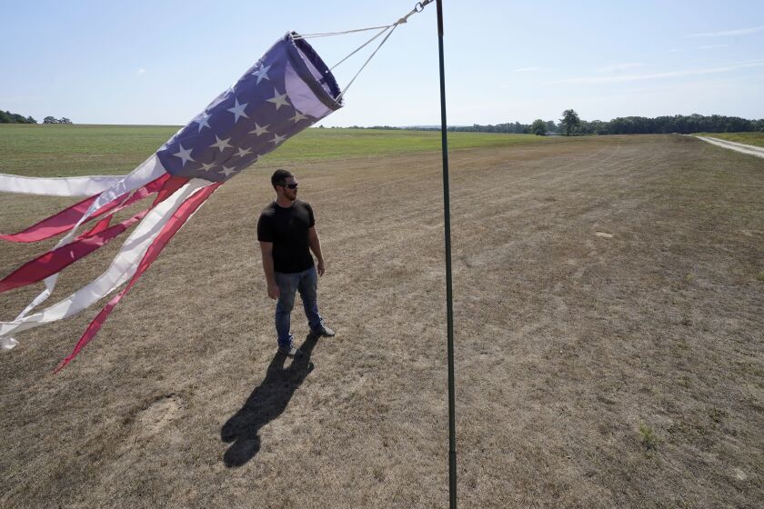 Hay farmer Milan Adams stands in a dry hay field near a wind sock, left, in Exeter, R.I., Tuesday, Aug. 9, 2022. Adams said in prior years it rained in the spring. This year, he said, the dryness started in March, and April was so dry he was nervous about his first cut of hay. (AP Photo/Steven Senne)