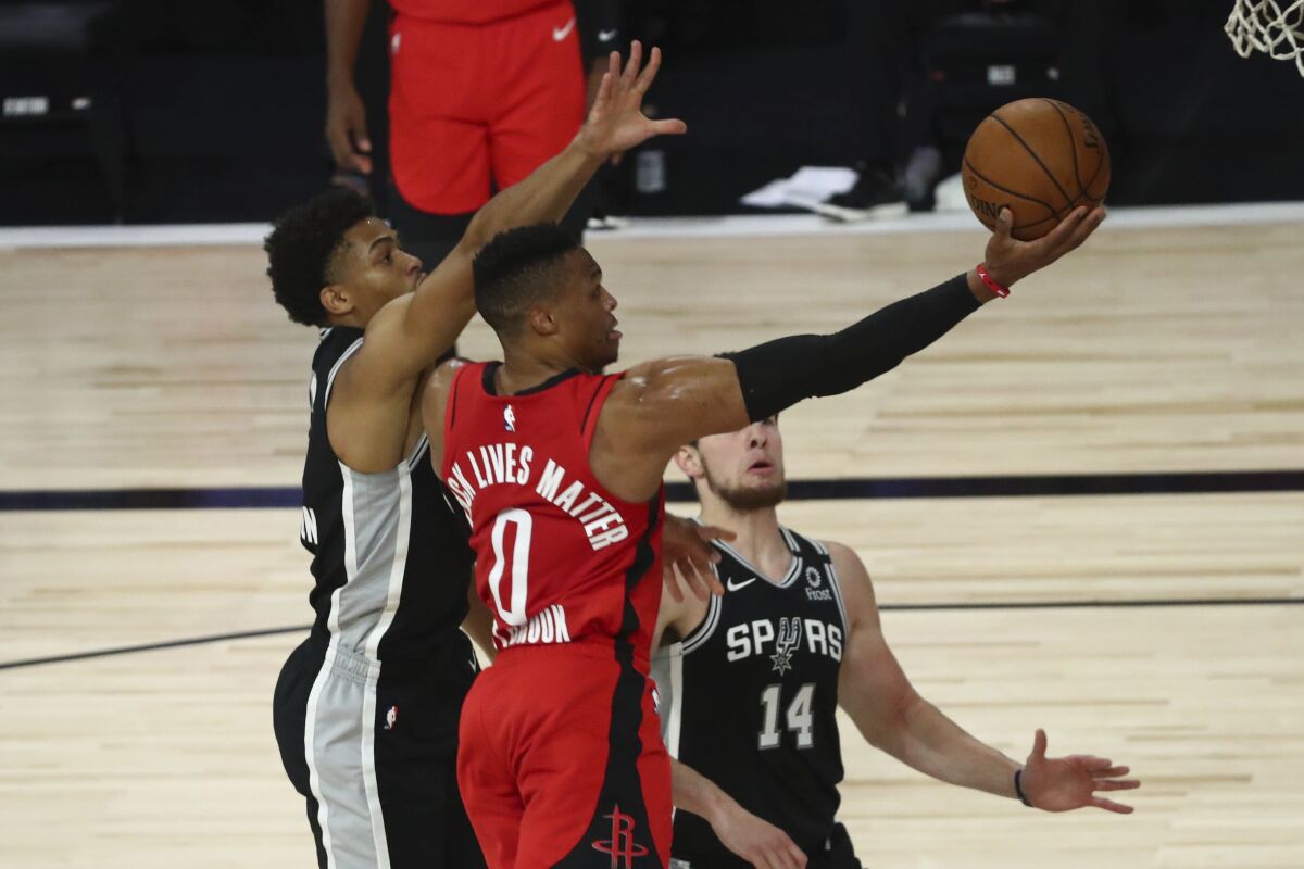 Houston Rockets guard Russell Westbrook, center, goes up for a shot while San Antonio Spurs forward Keldon Johnson, left, defends during the first half of an NBA basketball game Tuesday, Aug. 11, 2020, in Lake Buena Vista, Fla. (Kim Klement/Pool Photo via AP)