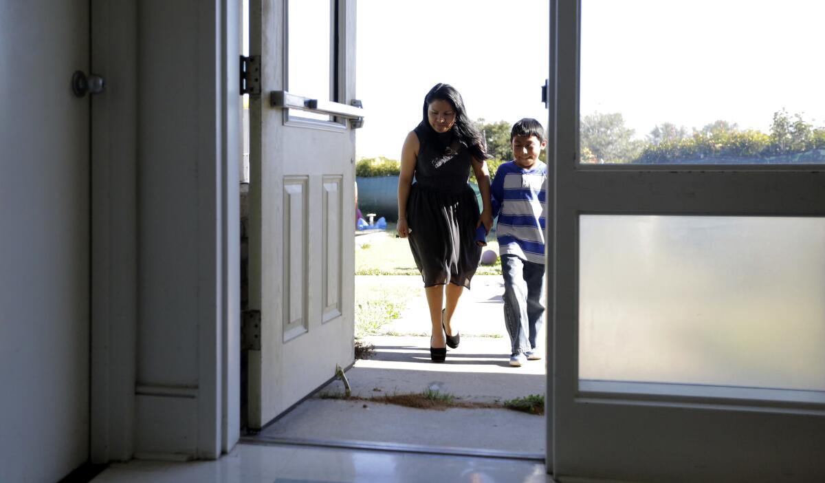 A woman and boy hold hands as they walk in from outside.