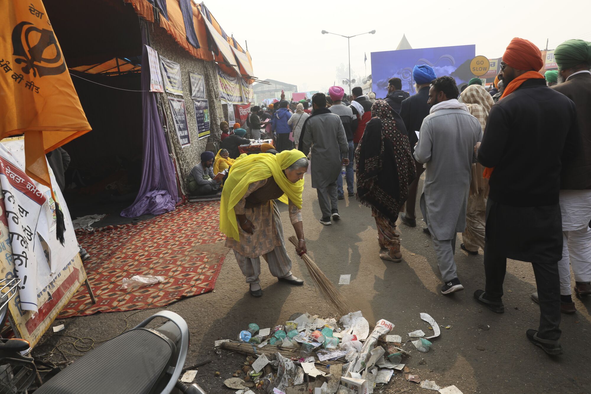 An elderly female farmer sweeps a road as she participates in a protest against new farm laws