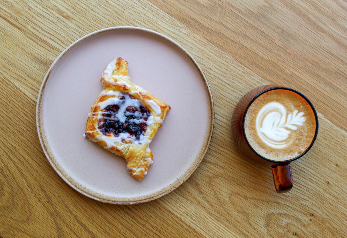 An overhead photo of a danish with a latte in an amber glass mug.