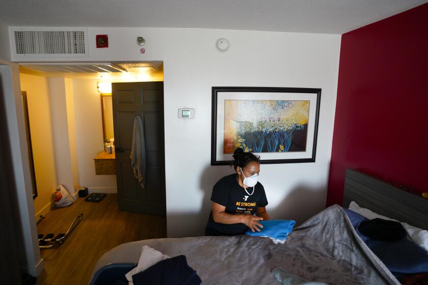 National City, CA - March 21: Marcela Ralac tidies up the hotel room at the Ramada Hotel in National City. Ralac and her husband, along with their 22-year-old son, share a single room. Ralac works as a housekeeper, and her husband works as a landscaper, as their son is a senior at SDSU and is expected to graduate this year. (Nelvin C. Cepeda / The San Diego Union-Tribune)
