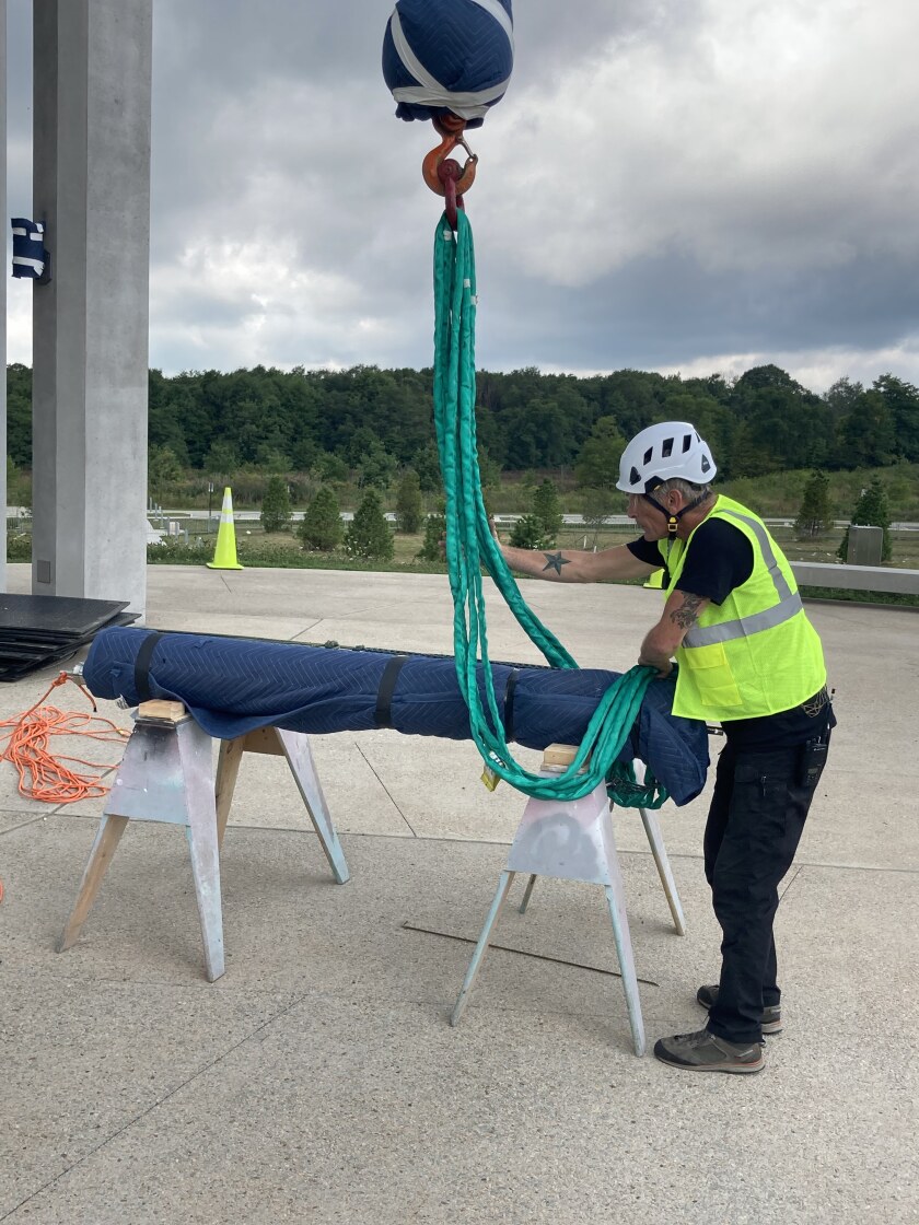 A man ties rope around a chime covered in protective blankets as it is prepared to be hoisted into the tower