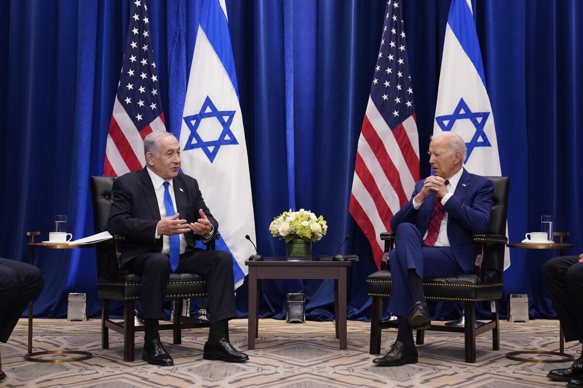 Israeli Prime Minister Benjamin Netanyahu and President Biden sit in front of dark blue curtains and U.S. and Israeli flags