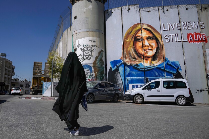 A person in a veil walks past a mural of slain journalist Shireen Abu Akleh.