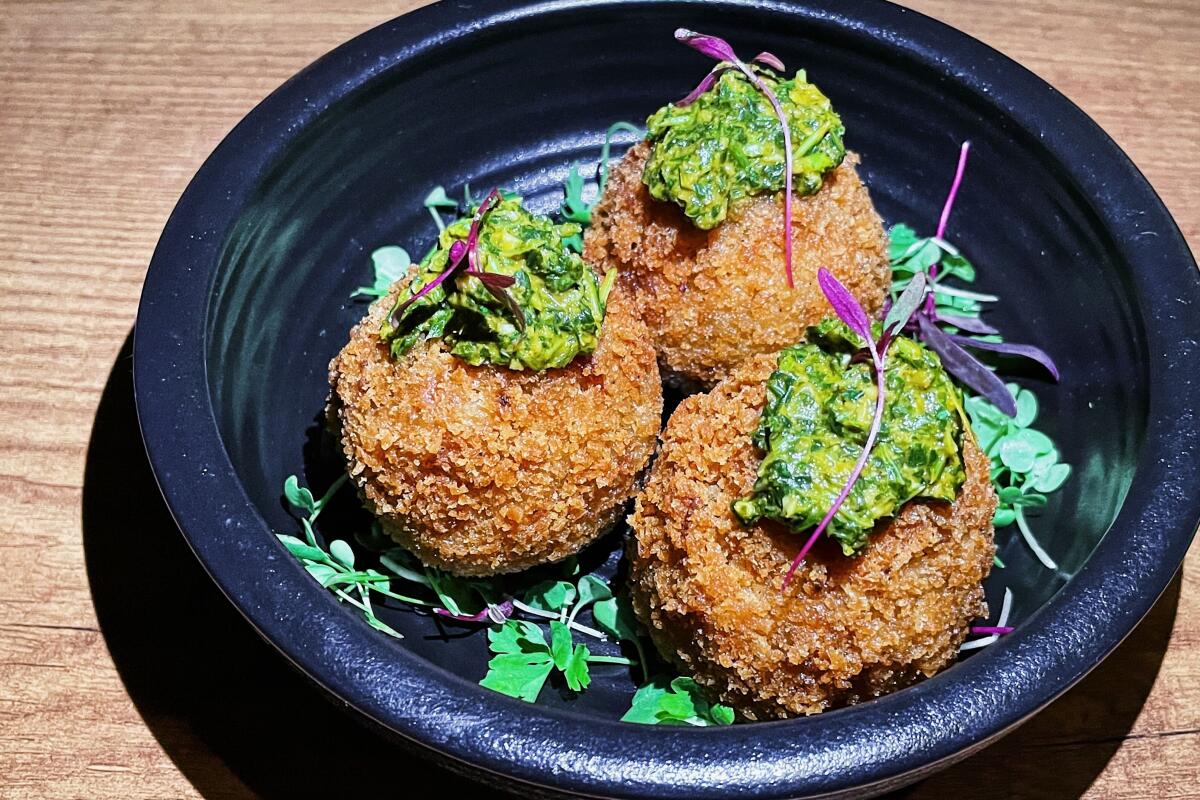 A trio of herb-topped jollof arancini in a black bowl from Ubuntu restaurant on Melrose