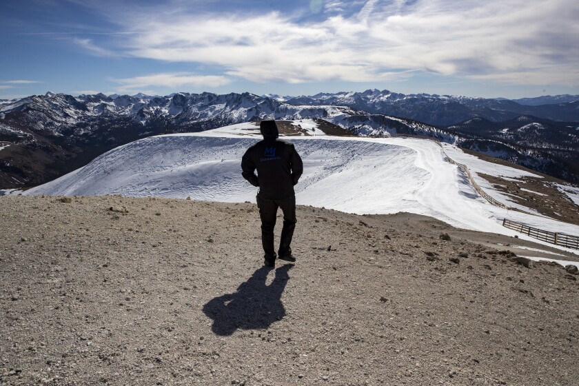 A man stands among gravel and patchy snow at the top of a mountain 