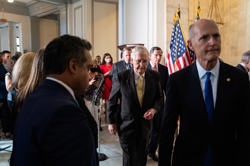 Senate Minority Leader Mitch McConnell and Sen. Rick Scott walk down a hall among other people