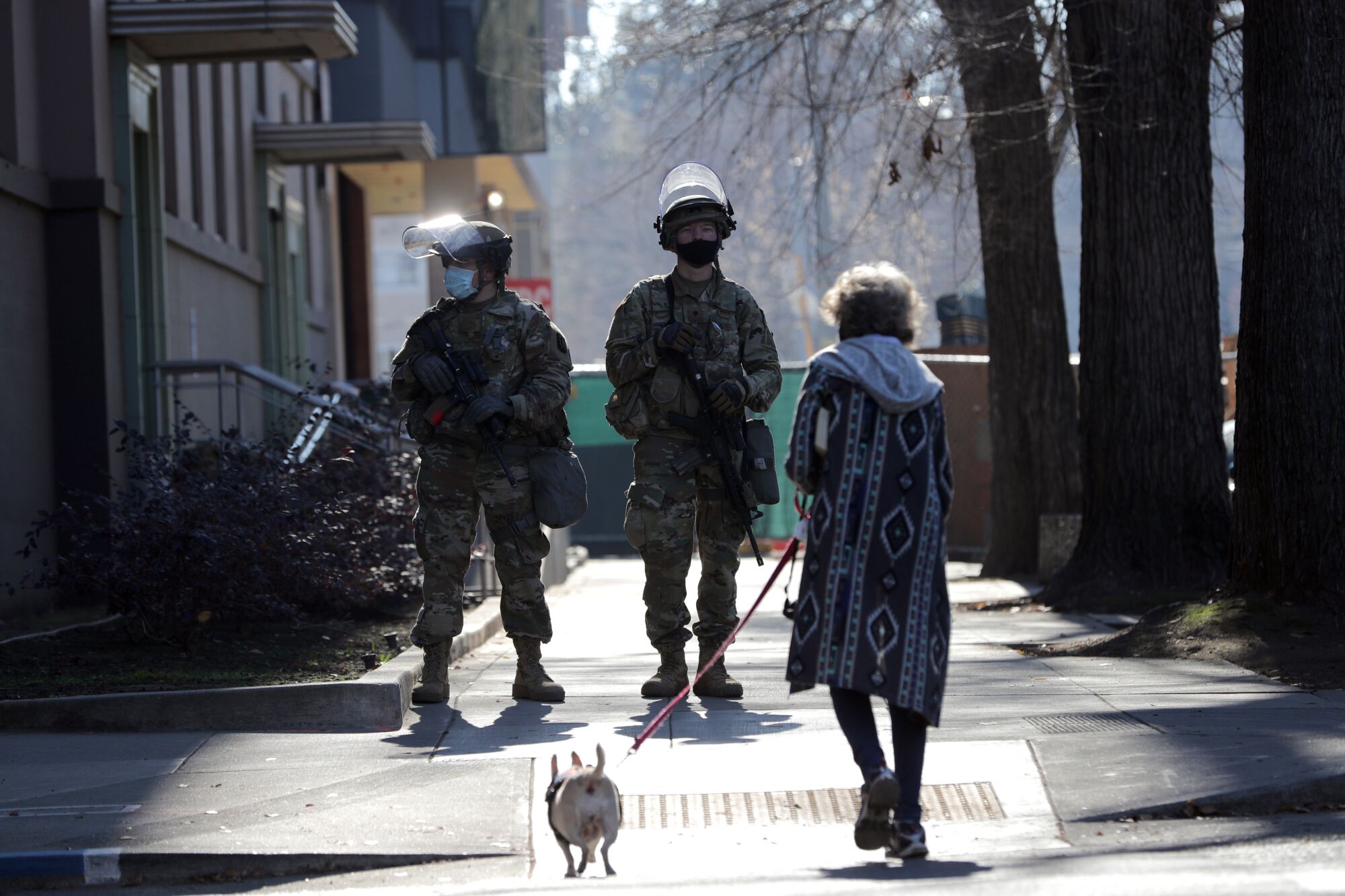 A woman walks her dog past armed National Guardsmen near the California Capitol.