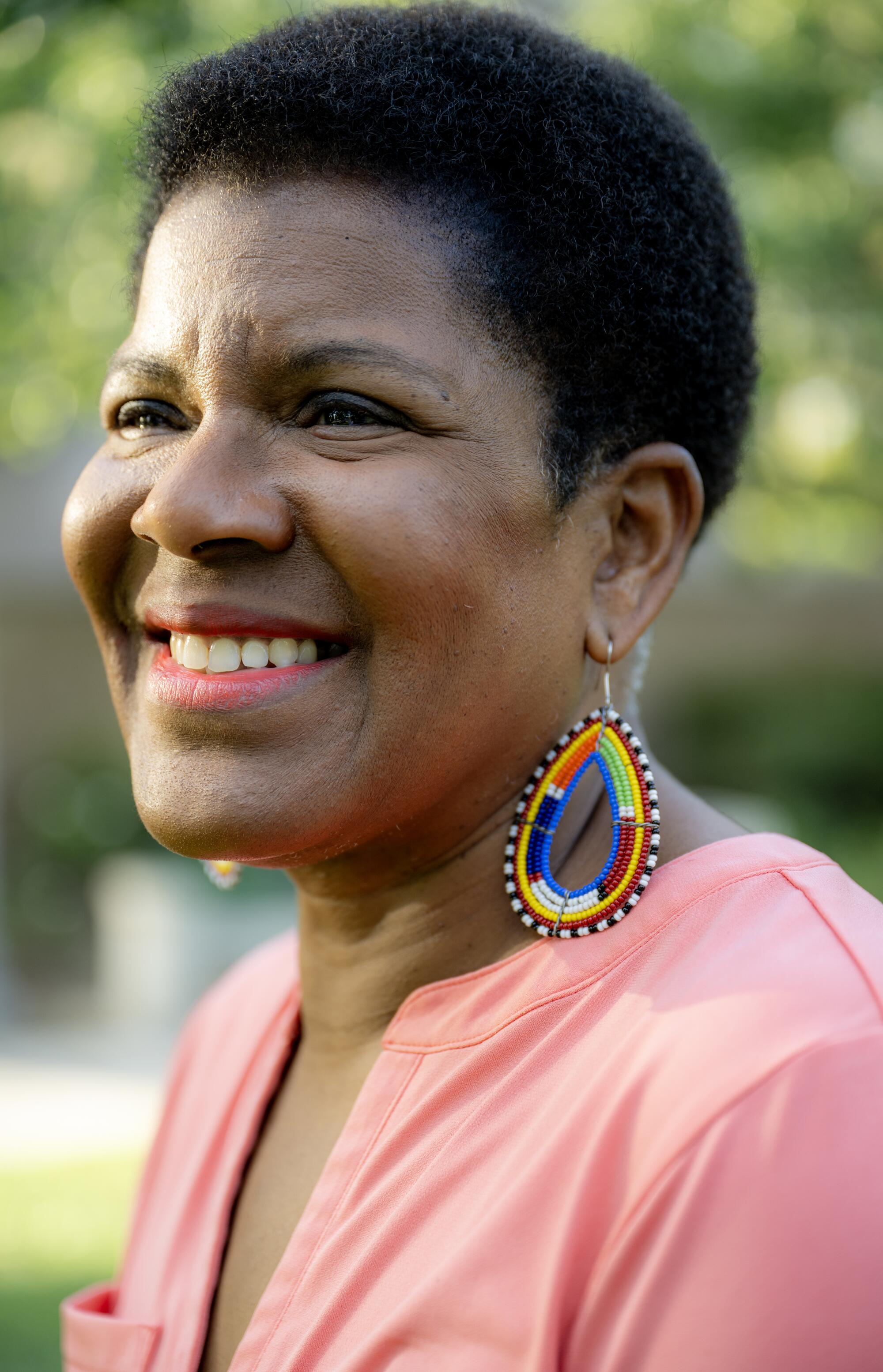 A smiling woman in a pink shirt with big teardrop earrings.