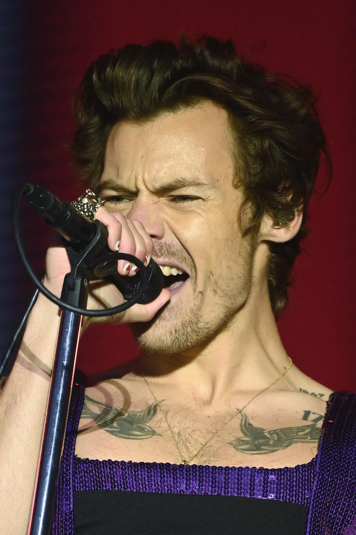 A man with tattoos on his chest sings ardently into a microphone