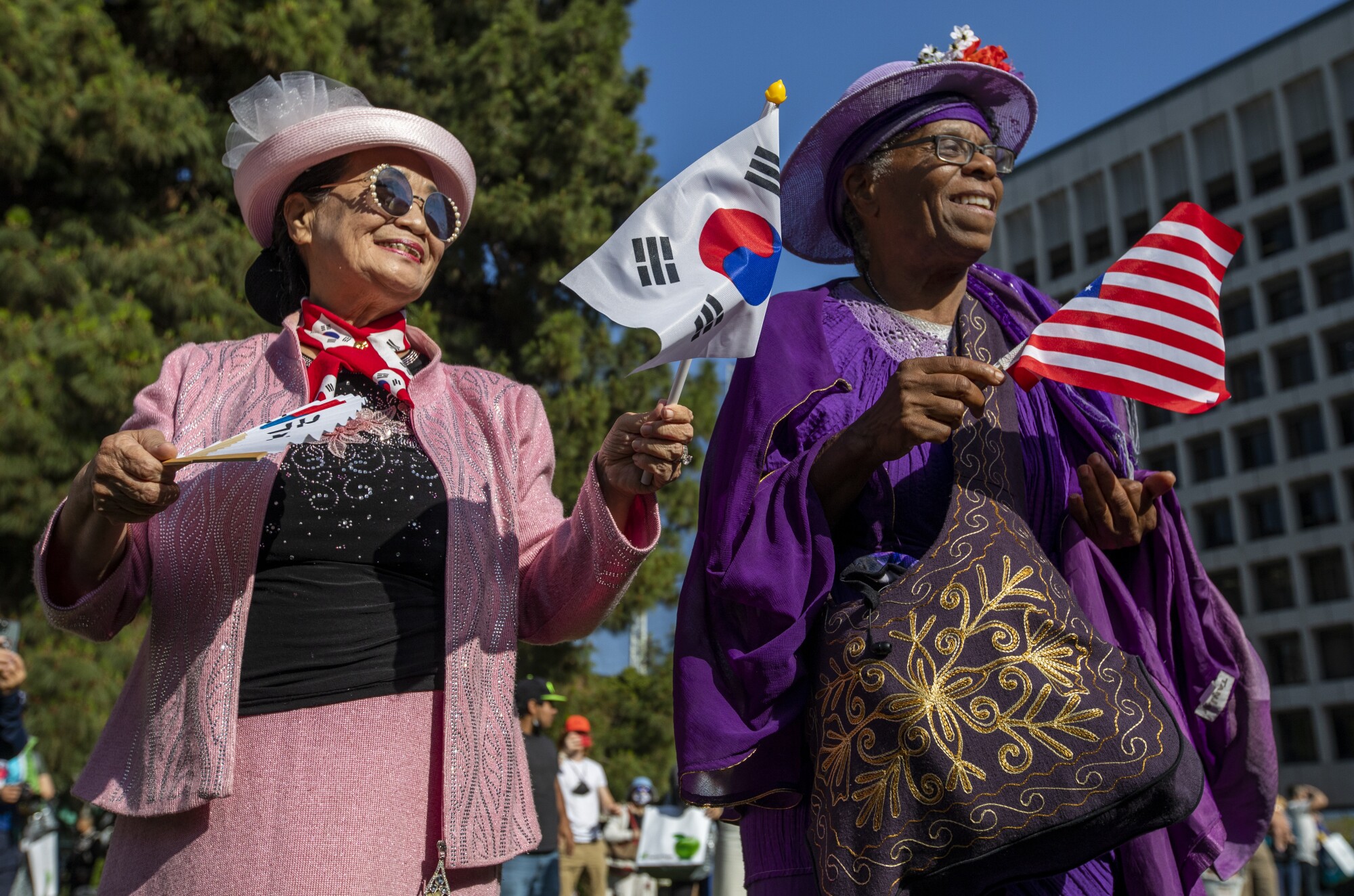 Two older women dressed in colorful colors hold small flags in their hands. 