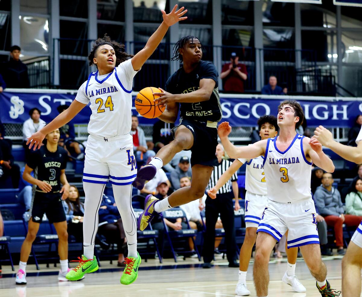 Amiri Meadows of St. John Bosco goes airborne as La Mirada's Gene Roebuck, left, and Julien Gomez provide pressure.