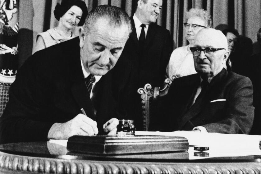 FILE - In this July 30, 1965 file photo, President Lyndon Johnson signs the Medicare Bill into law while former President Harry S. Truman, right, observes during a ceremony at the Truman Library in Independence, Mo. At rear are Lady Bird Johnson, Vice President Hubert Humphrey, and former first lady Bess Truman. When Johnson signed Medicare and Medicaid into law Americans 65 and older were the age group least likely to have health insurance. (AP Photo)