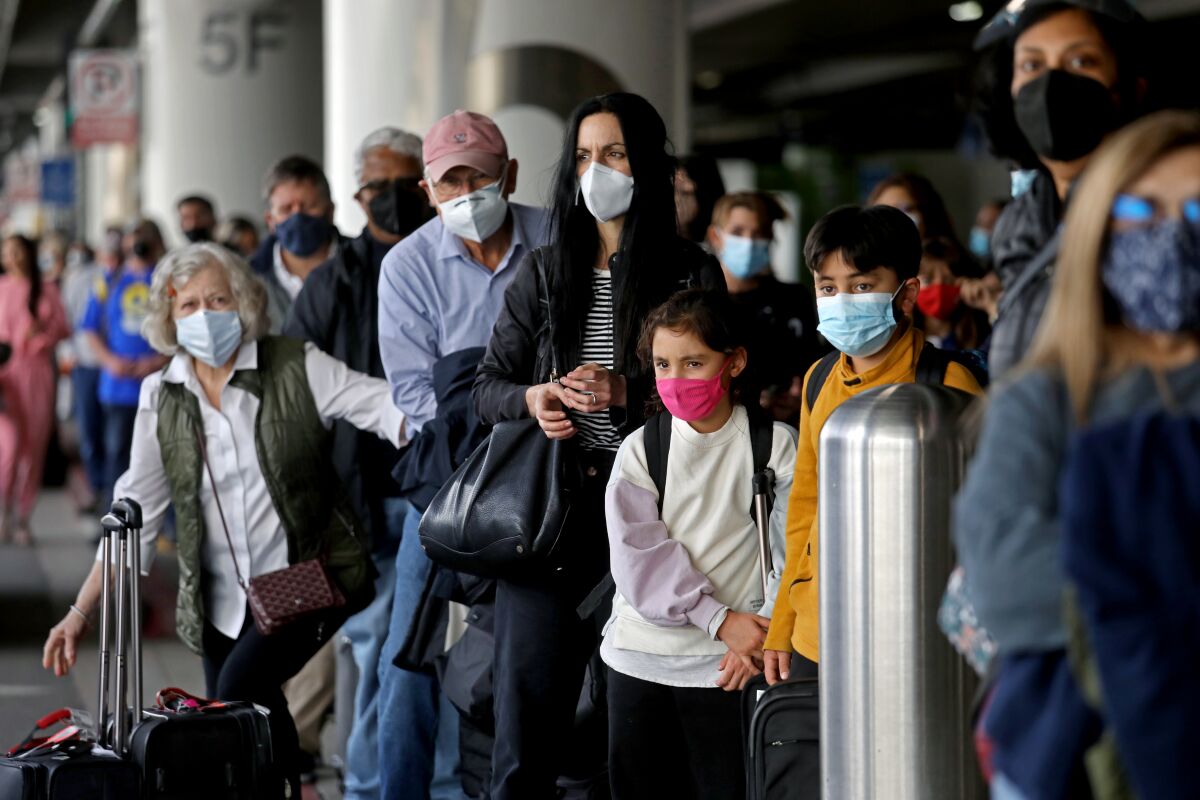 Passengers wear masks while waiting in line at an airport.