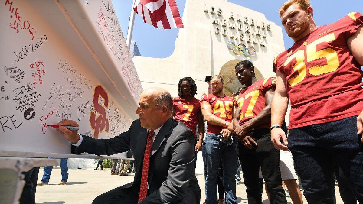 USC head coach Clay Helton signs a metal beam during a media tour of the Coliseum.