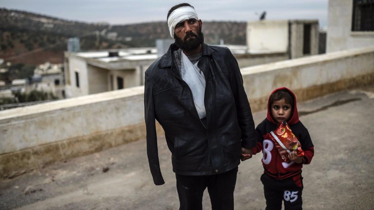 An injured Syrian man who just arrived in the Syrian town of Bab al-Hawa on the border with Turkey waits with his child outside a hospital on Dec. 16, 2016.