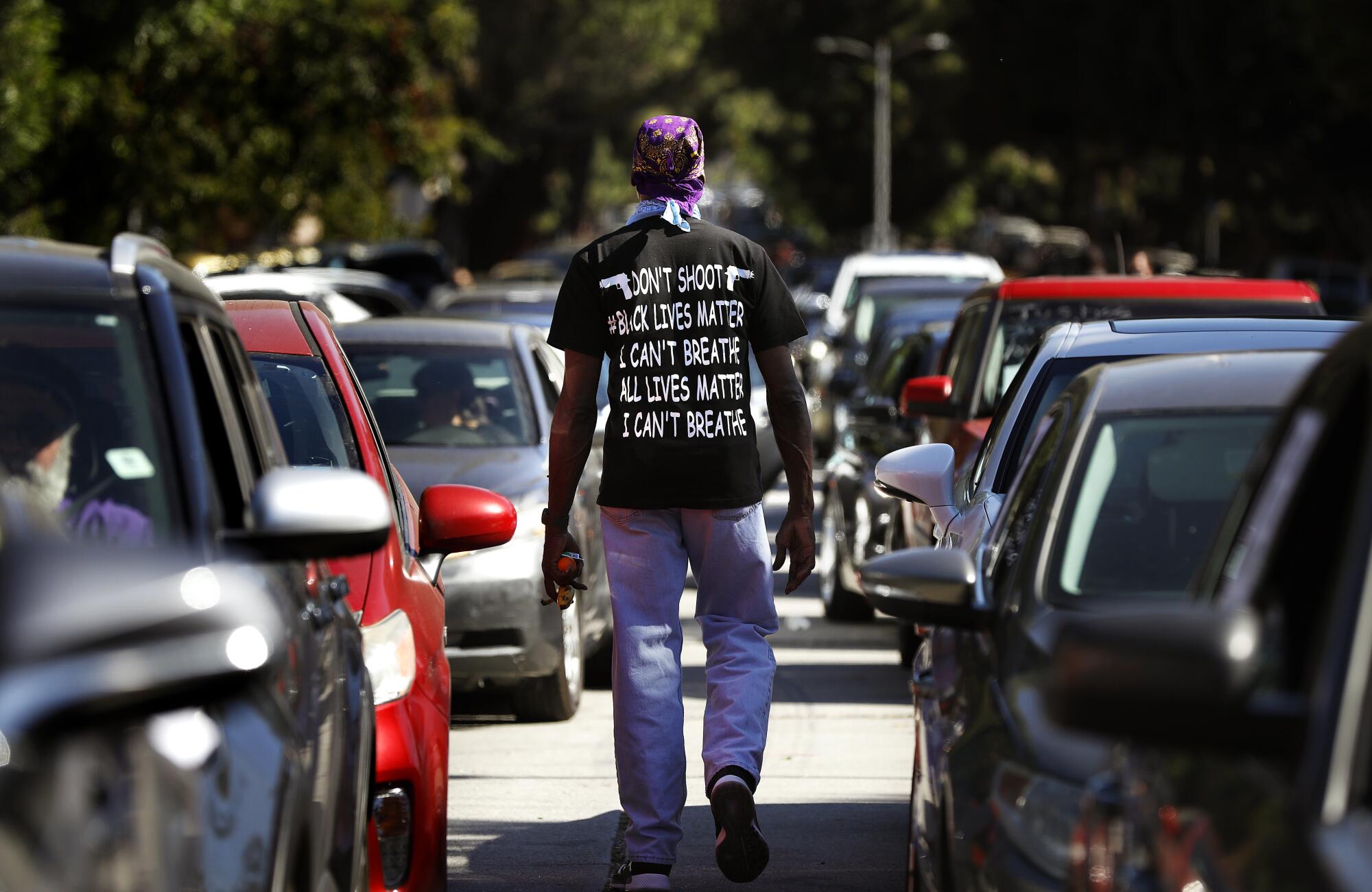 Morris Griffin walks between cars before a procession leaves Leimert Park for a memorial service to honor George Floyd.
