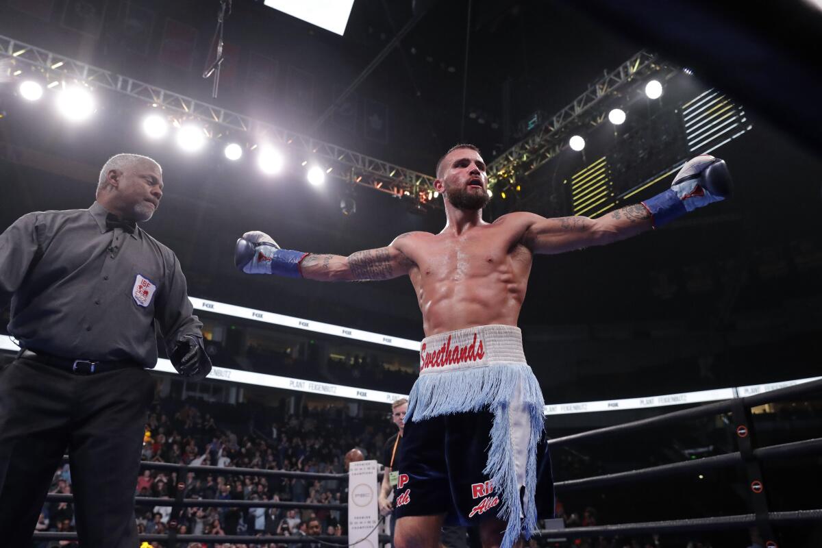 Caleb Plant holds his arms out by his sides in the ring while a referee stands next to him