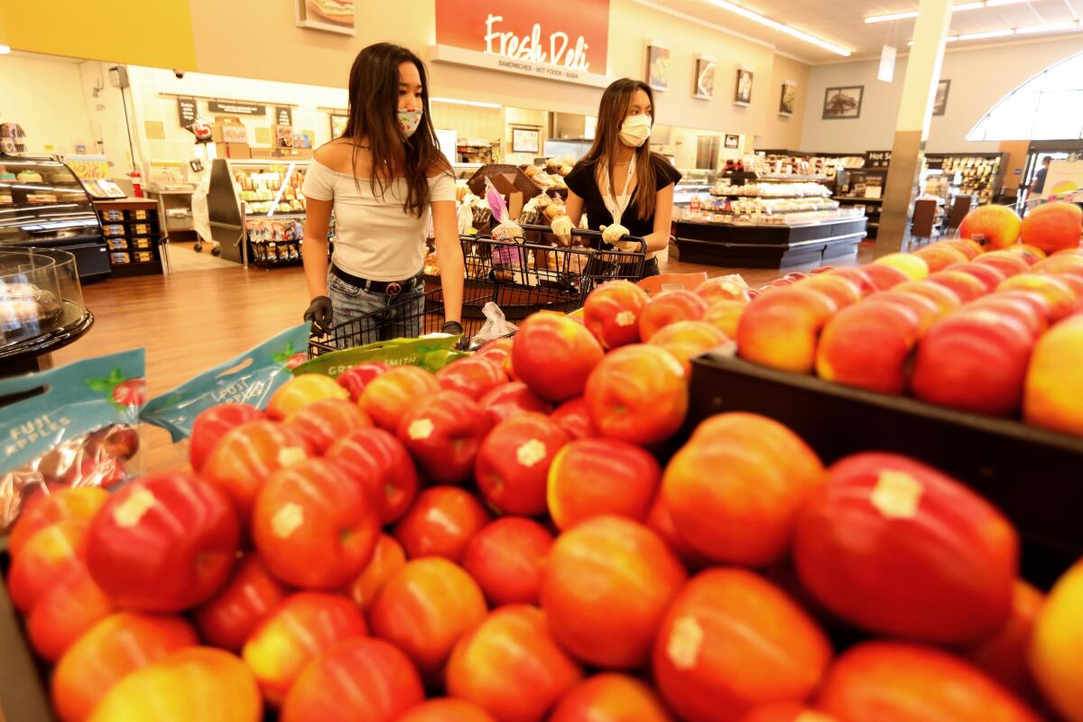 Sharia Busnawi, 16, left, and Krysta Mendoza, 17, juniors at West Ranch High School, shop for groceries at an Albertsons store in Valencia while volunteering for the Six Feet Supplies service.