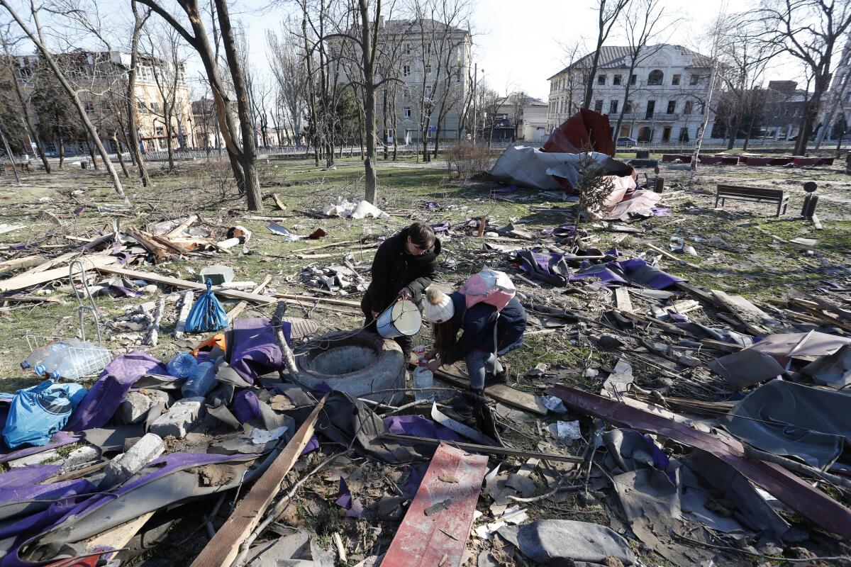 People stand over a well with buckets, surrounded by debris, in Ukraine.