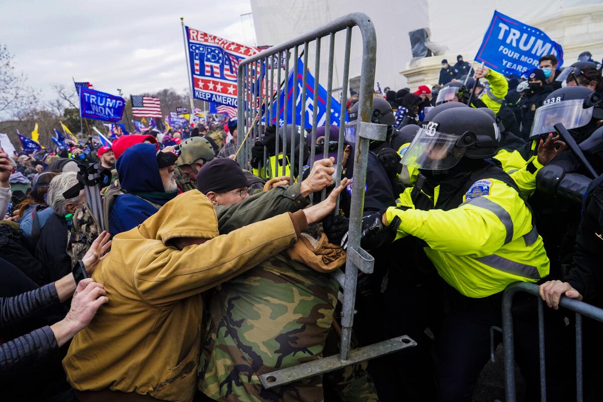 A crowd pushes a metal barricade up against a group of police in riot gear
