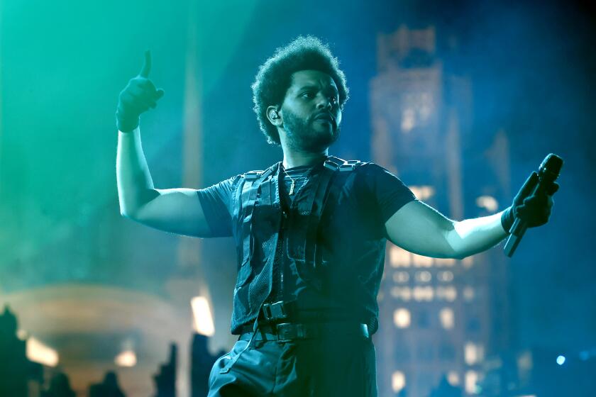 man, the weeknd, with frizzed afro, performing on sofi stadium stage, wearing tactical vest and black shirt, pants and gloves