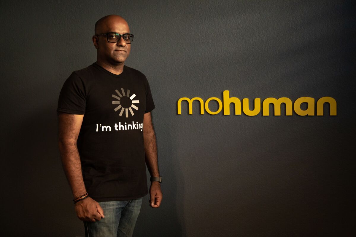 Nishal Mohan, standing against a dark grey wall with the name of his nonprofit, mohuman, in yellow on the wall