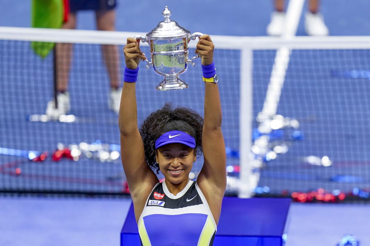 Naomi Osaka holds up the championship trophy on a tennis court.