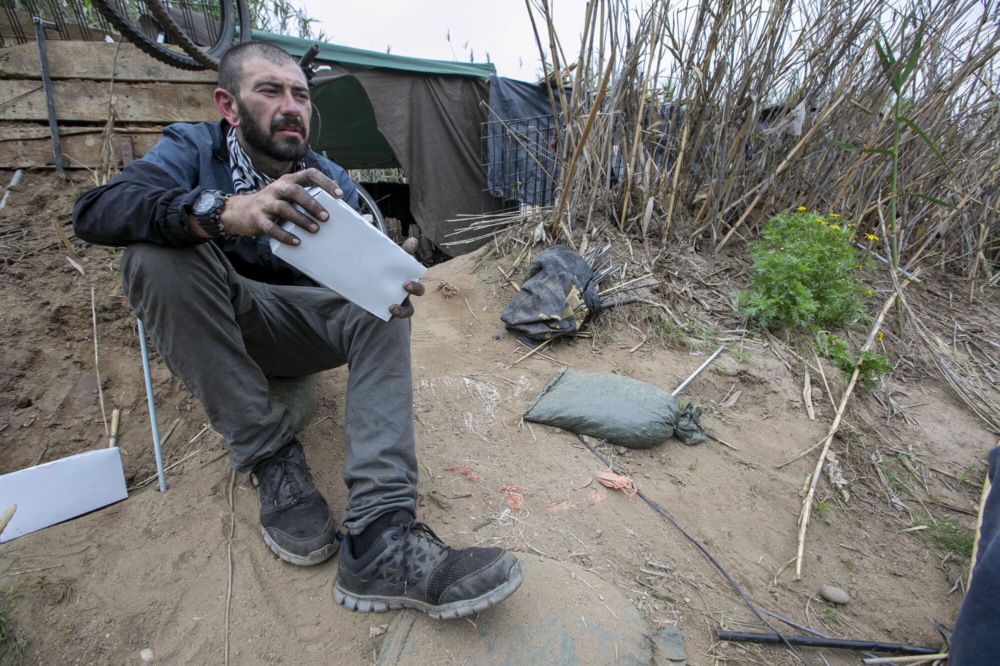 Brandon Nerz, who is experiencing homelessness and lives in "The Jungle" sat outside of his camp after getting a meal and hygiene kit from Alpha Project outreach workers Anthony Aquiningoc and Nick Healy on Thursday, April 30, 2020.