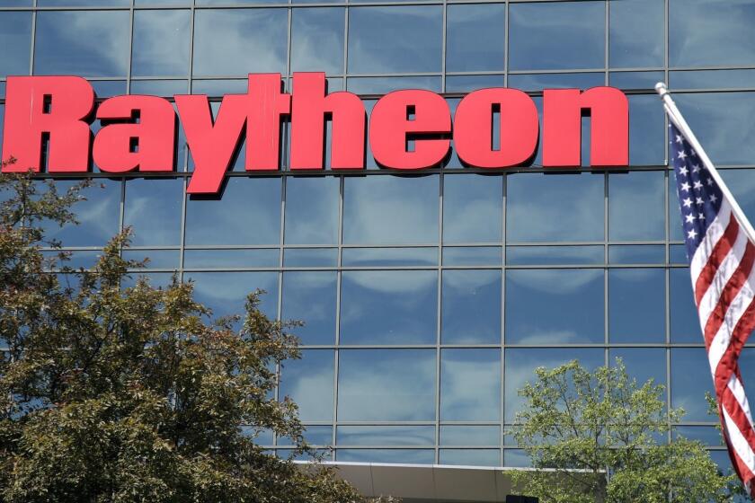 And American flag flies in front of the facade of Raytheon's Integrated Defense Systems facility, Monday, June 10, 2019, in Woburn, Mass. Raytheon Co. and United Technologies Corp. are merging in a deal that creates one of the world's largest defense companies. (AP Photo/Elise Amendola)