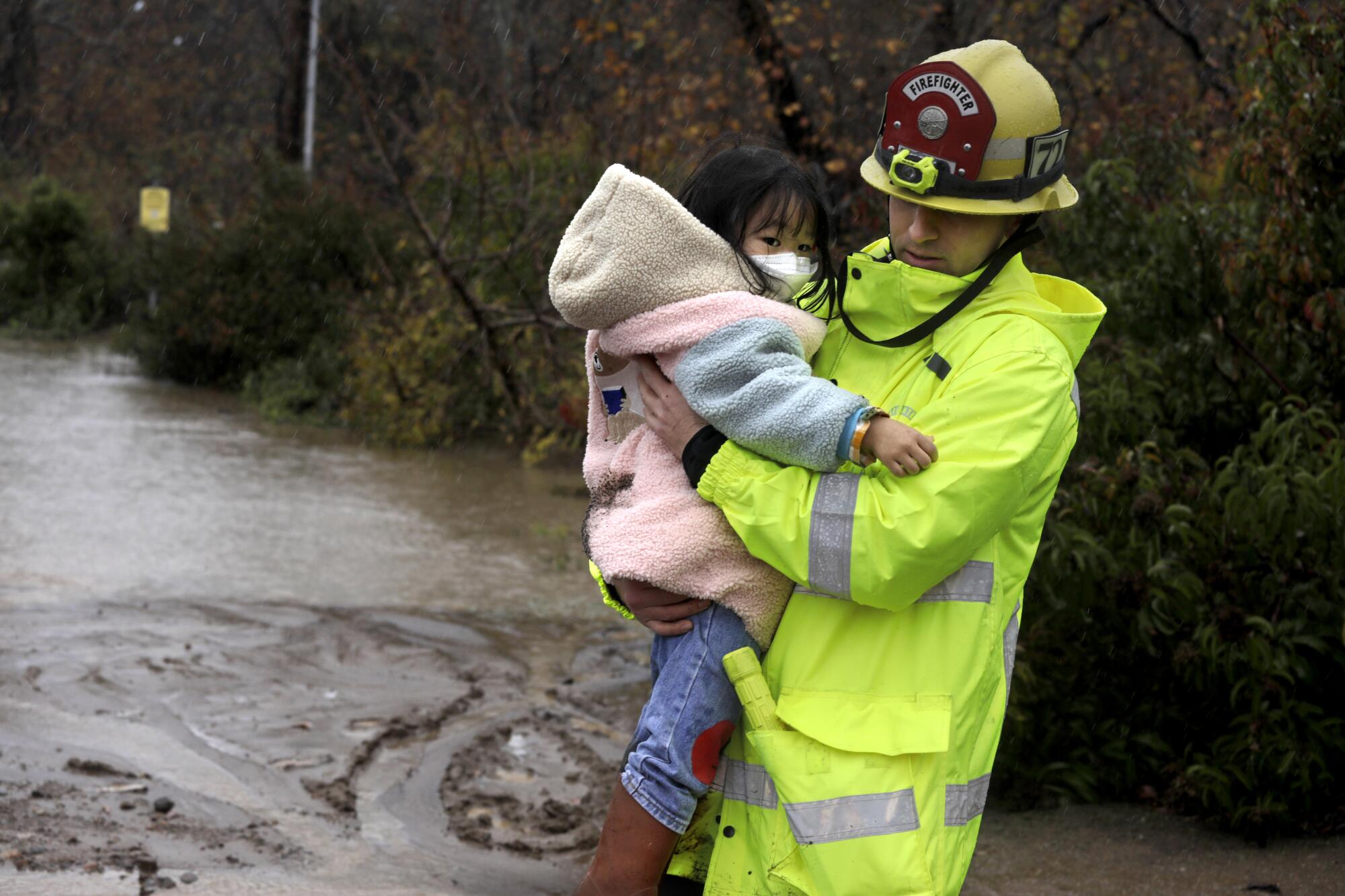 A firefighter helps evacuate Evelyn Jung, and her family from a flooded area at the Leo Carrillo Campground 