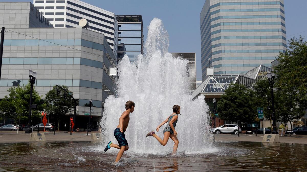 Langstrom Kalstrom, left, and Violet Dashney run through the Salmon Street Springs fountain in Portland, Ore., as the city endured triple-digit heat.