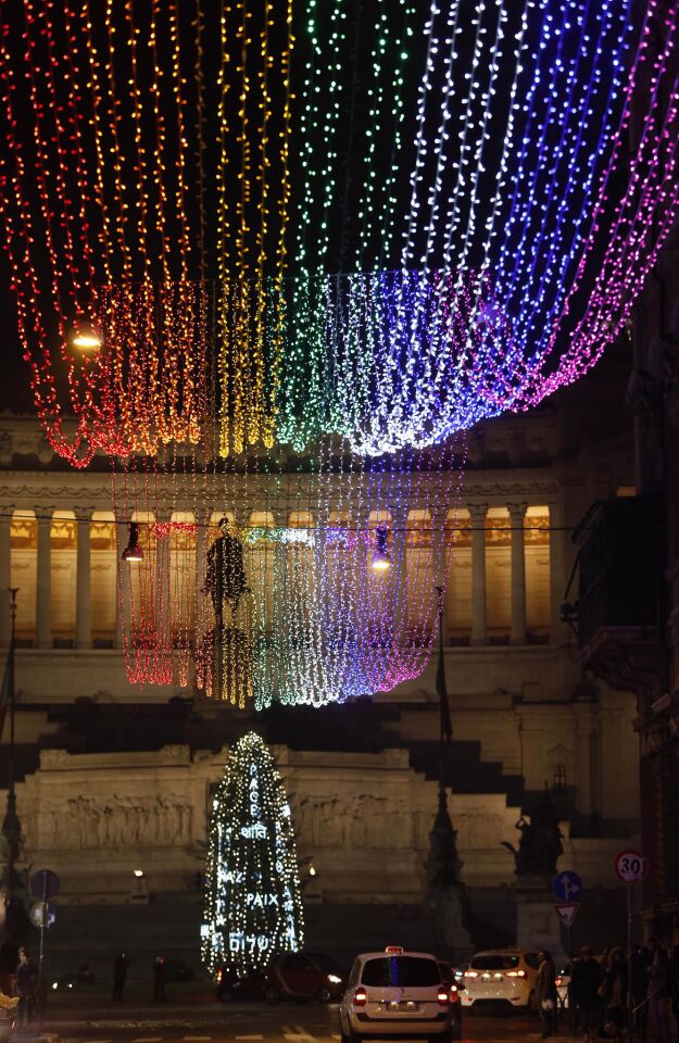 The Via del Corso is decorated with rainbow lights, ending at a Christmas tree decorated with multicultural spellings of the word "peace." The lights are dedicated to the late South African icon Nelson Mandela.