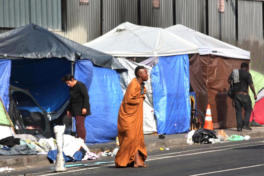 LOS ANGELES, CA - JUNE 14, 2024 - Homeless make their way in front of a row of tents along 5th Street in Skid Row in Los Angeles on June 14, 2024. (Genaro Molina/Los Angeles Times)