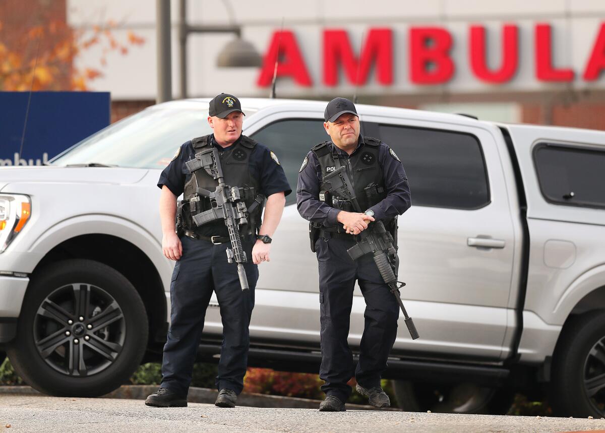 Two police officers with guns stand in front of a truck. 