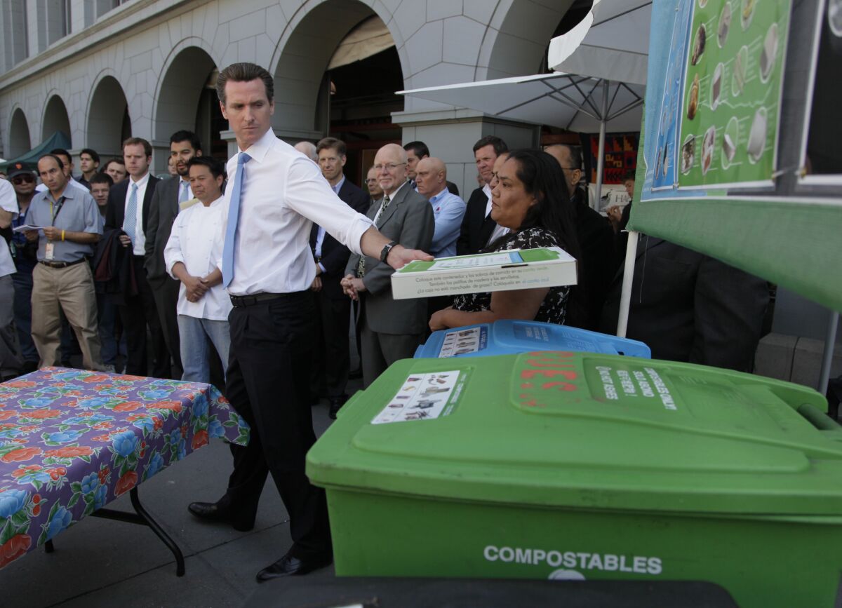 Then-San Francisco Mayor Gavin Newsom places a compostable pizza box on  a bin.