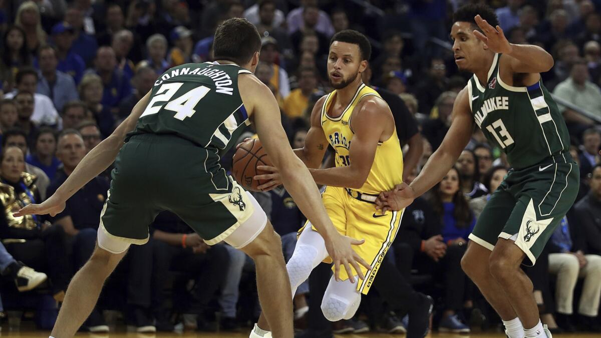 Golden State Warriors' Stephen Curry, center, drives the ball between Milwaukee Bucks' Pat Connaughton (24) and Malcolm Brogdon, right, during the first half.