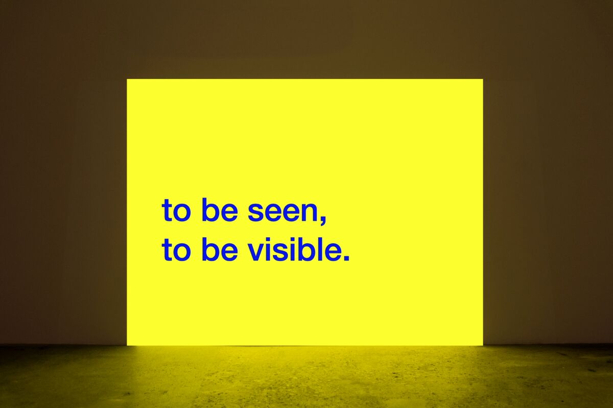 Tony Cokes, "Evil.13.5 (4 OE)," 2022. Neon yellow projection with "to be seen, to be visible" displayed on it.