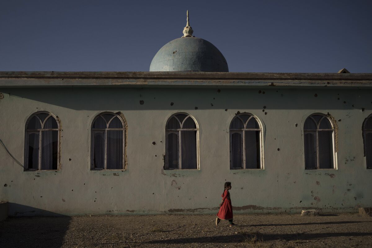 An Afghan girl walks outside a mosque marked by bullet holes at a village in Wardak province, Afghanistan, Monday, Oct. 11, 2021. (AP Photo/Felipe Dana)