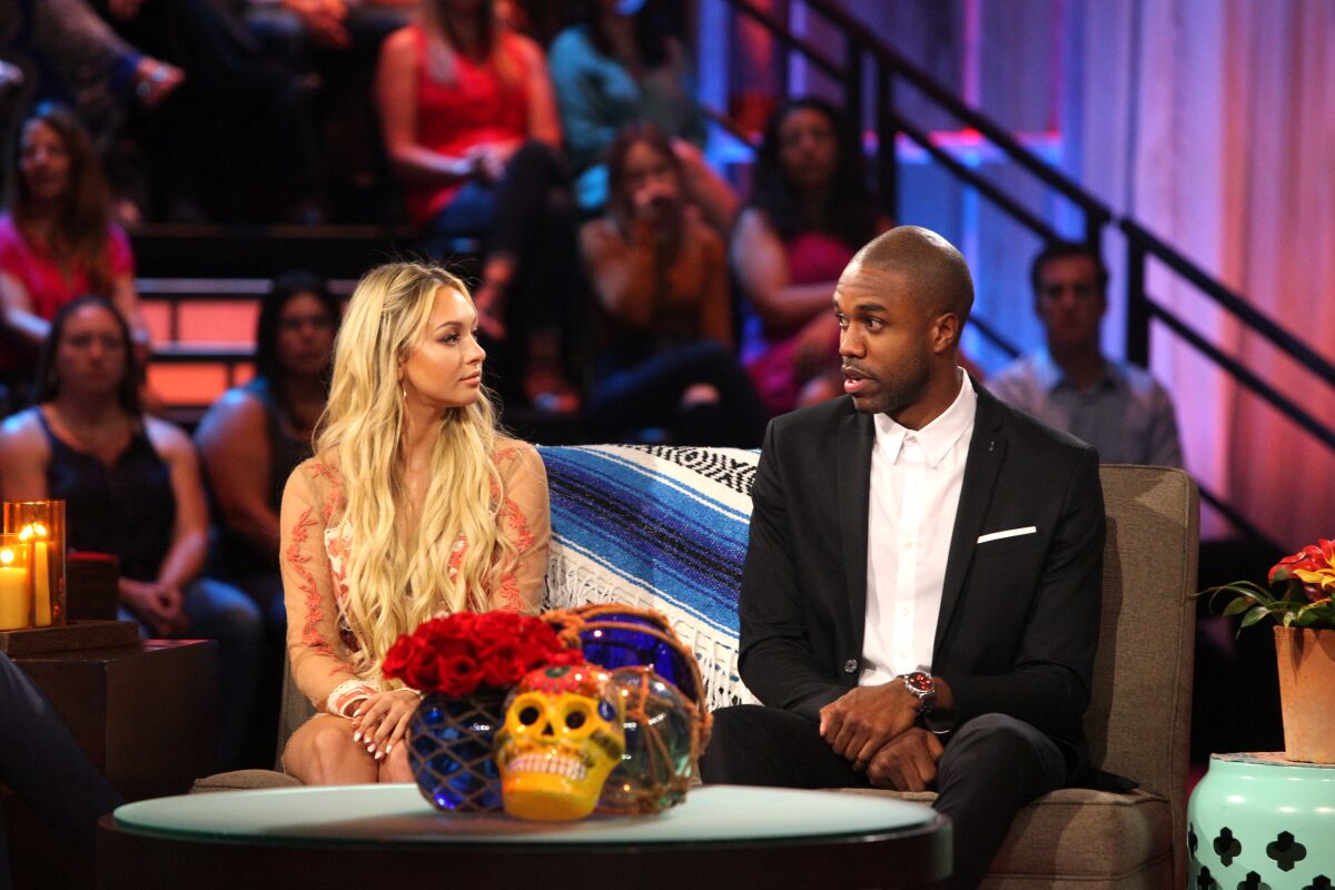 A woman with blond hair stares at a man in a blazer talking in front of a studio audience.