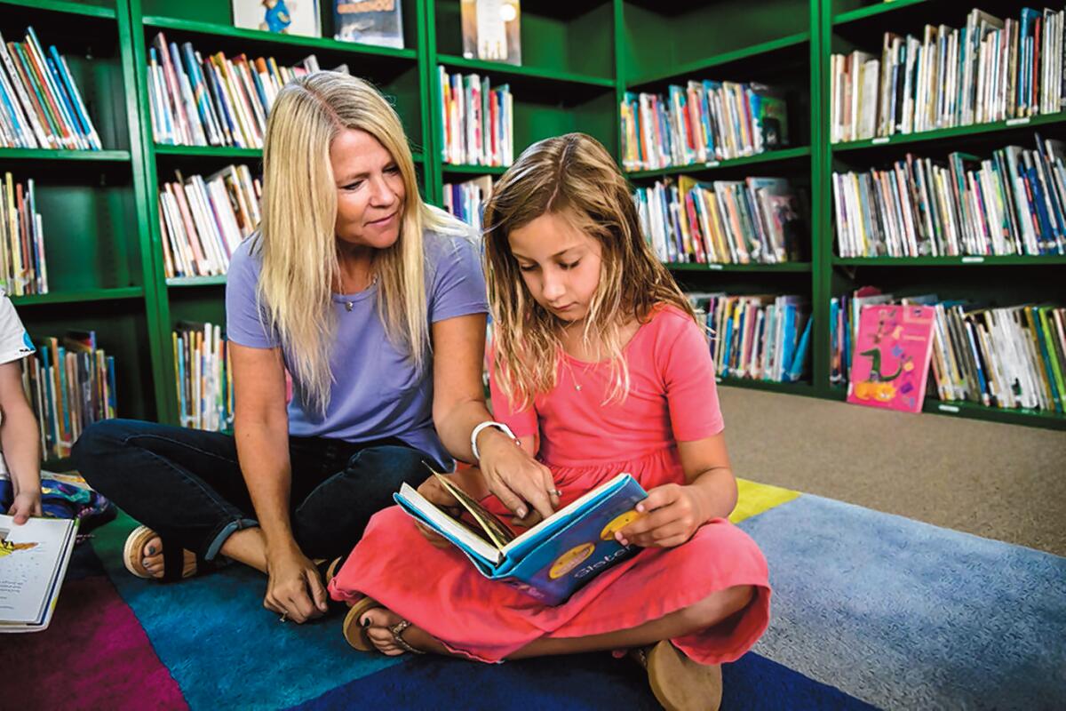 A teacher points to a page as a child reads.