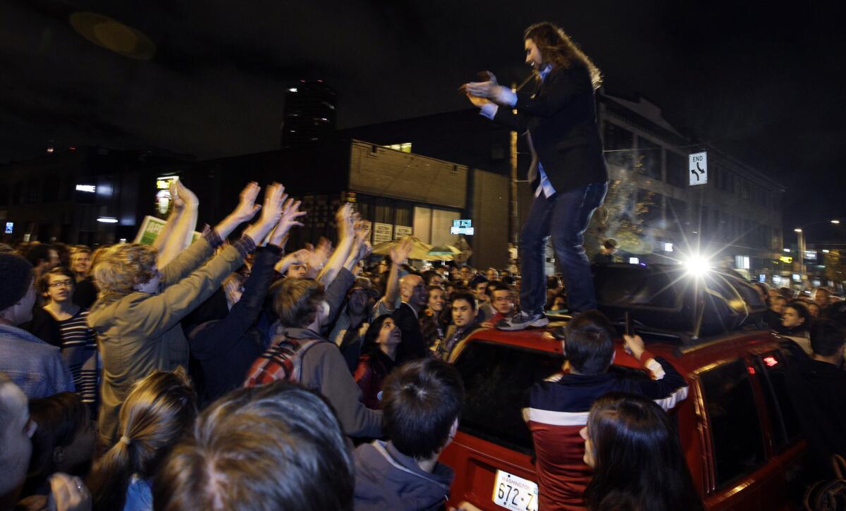 A man stands on a car and encourages a crowd gathered to celebrate the election results in Seattle's Capitol Hill.