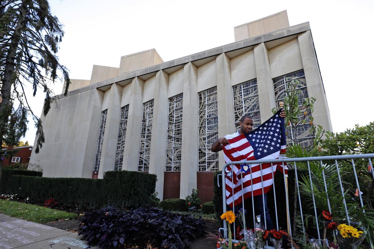 FILE-In this Oct. 27, 2019 file photo a man places an American flag outside the Tree of Life synagogue in Pittsburgh on the first anniversary of the shooting at the synagogue, that killed 11 worshippers. An evidentiary hearing in the case of Robert Bowers a western Pennsylvania truck driver accused of killing 11 people at the Pittsburgh synagogue in 2018, is expected to get underway inside a federal courtroom in Pittsburgh on Tuesday, Oct. 12, 2021. (AP Photo/Gene J. Puskar, File)