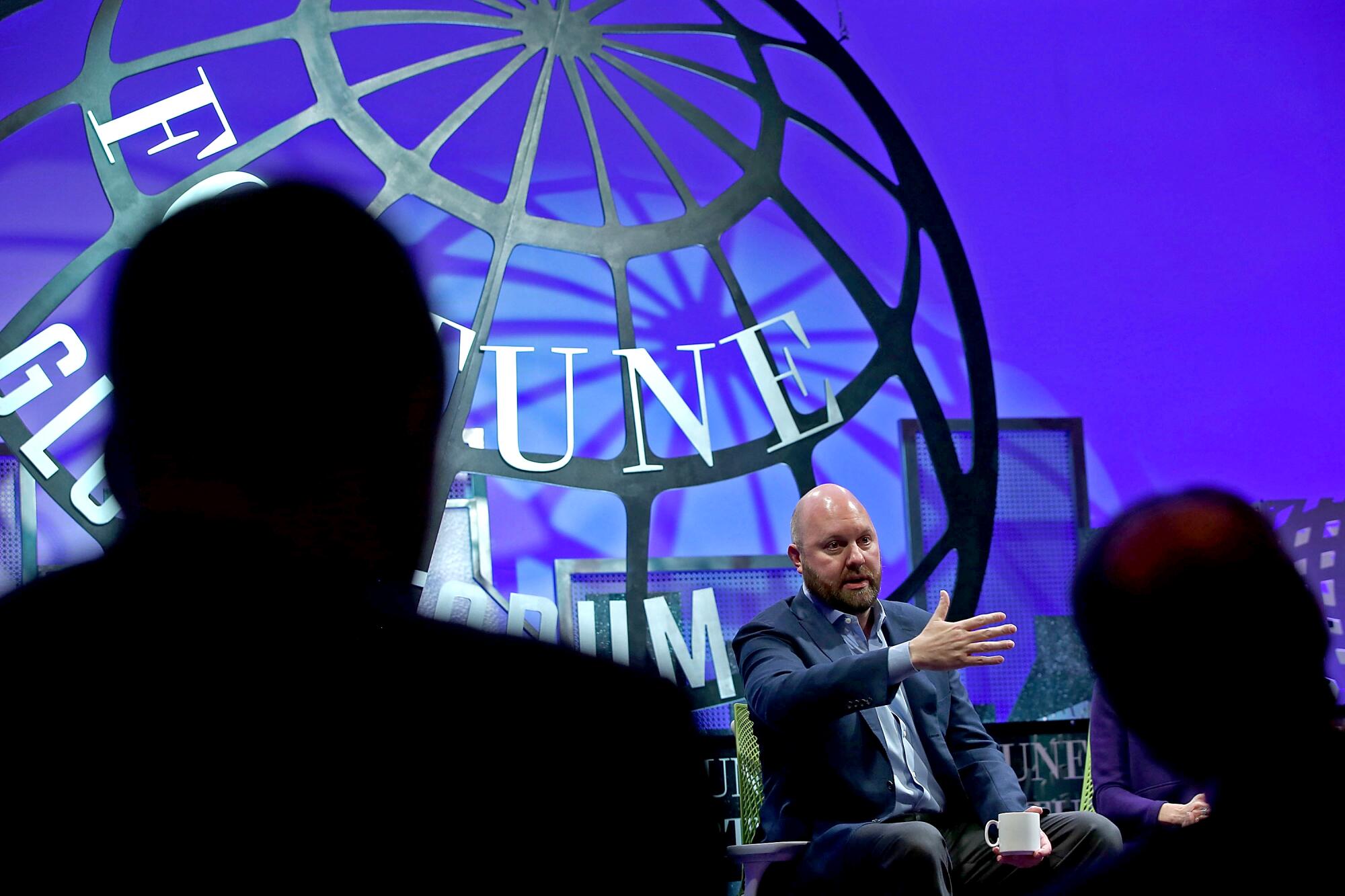 Marc Andreessen, bald man in a suit, seated at a panel in front of a frame of a globe.