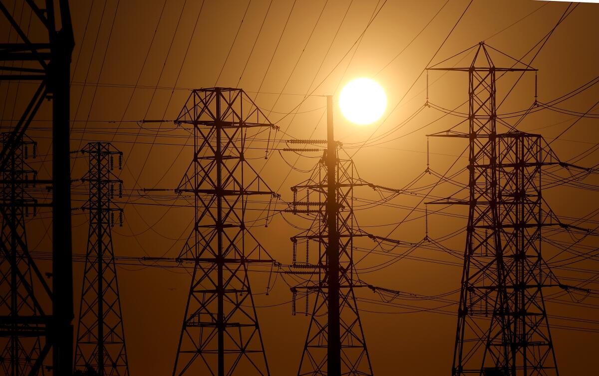 Structures holding power lines are seen amid hazy sky and orange sun.