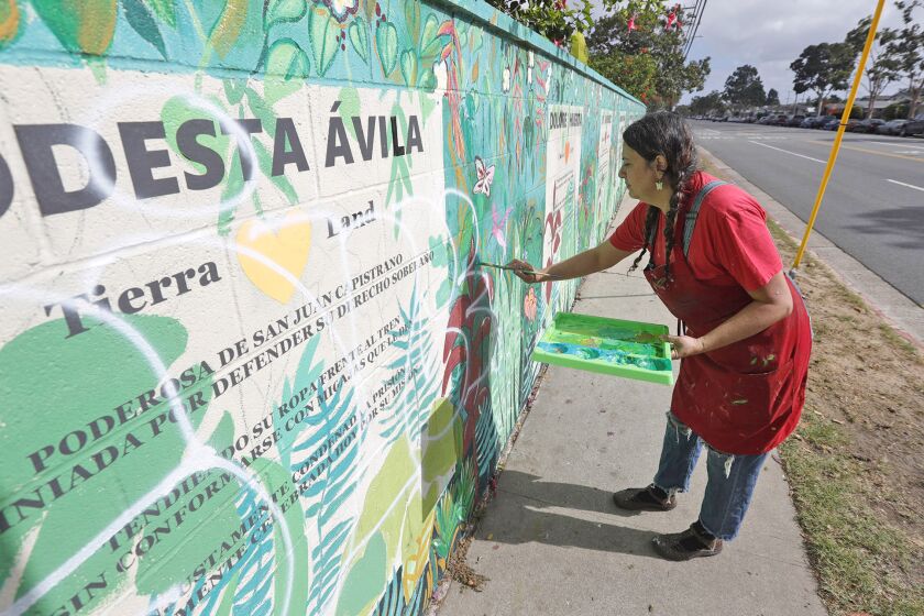 Artists and muralists Alicia Rojos paints over a vandals spray painted words "white power" on the Poderosas mural wall on Baker Street in Costa Mesa on Tuesday.