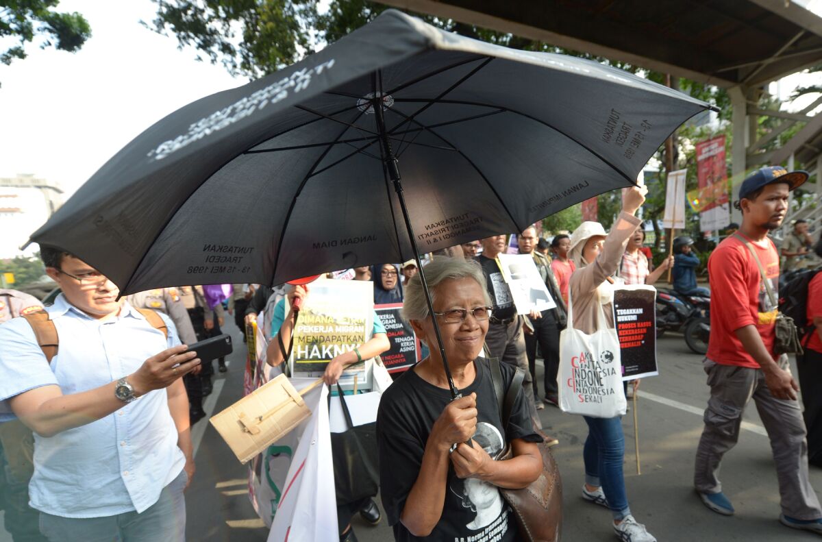 A woman with a large black umbrella amid a crowd of people, some holding signs 