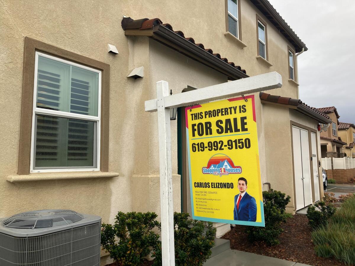 A "for sale" sign in front of a stucco home