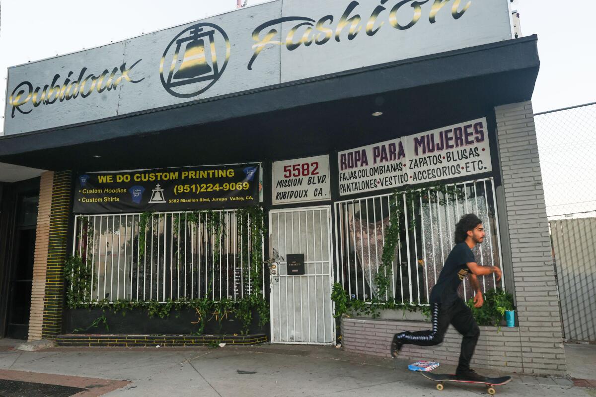 A person skateboards past Rubidoux Fashion, a Jurupa Valley store with bars on its windows